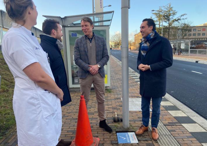Wethouder Arjen van Drunen en gedeputeerde Stijn Smeulders staan met een arts van het Amphia ziekenhuis bij de bushalte waar een rookvrije tegel gelegd is.