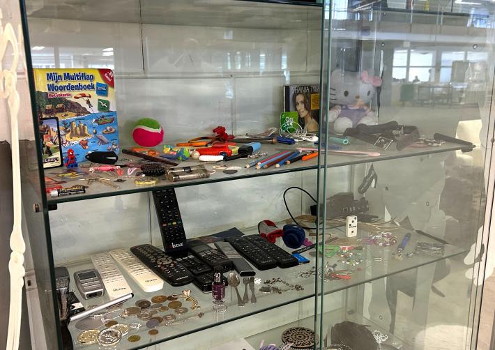 Een glazen vitrinekast met verschillende spullen. Onder andere afstandsbedieningen, munten, sieraden en speelgoed