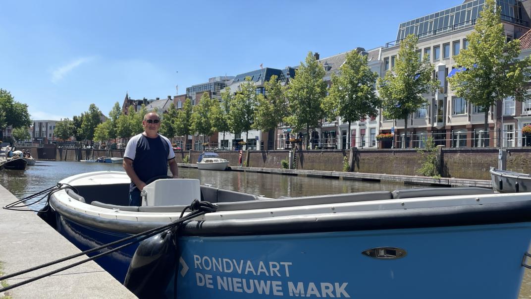 Johan staat aan boord van een blauwe sloep in de haven van Breda.